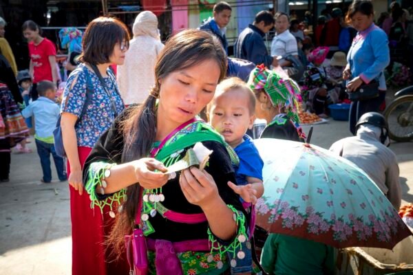 Young ethnic mom in traditional wear with baby and sticky rice in banana leaf in urban market